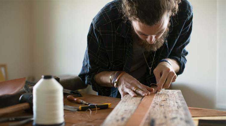 Man 制作 a belt on a table as a way to make money from home.